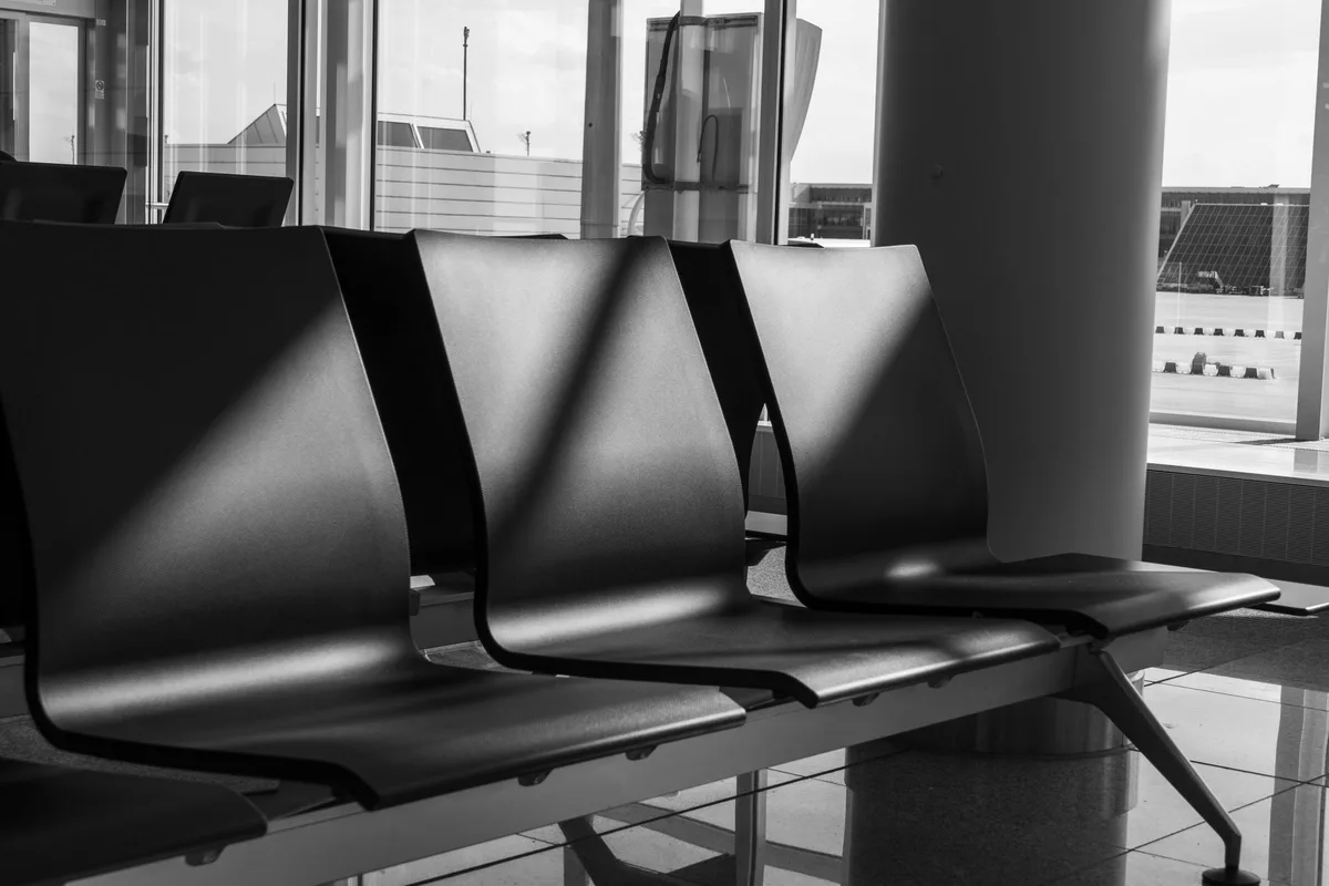 Empty waiting-room chairs in hard shadow, photographed in monochrome.