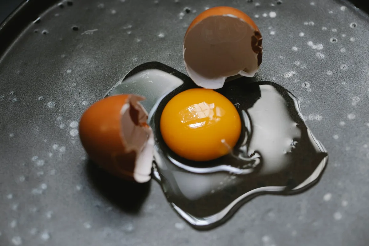 A cracked eggshell photographed in hard black and white, the fracture line lit from the side.