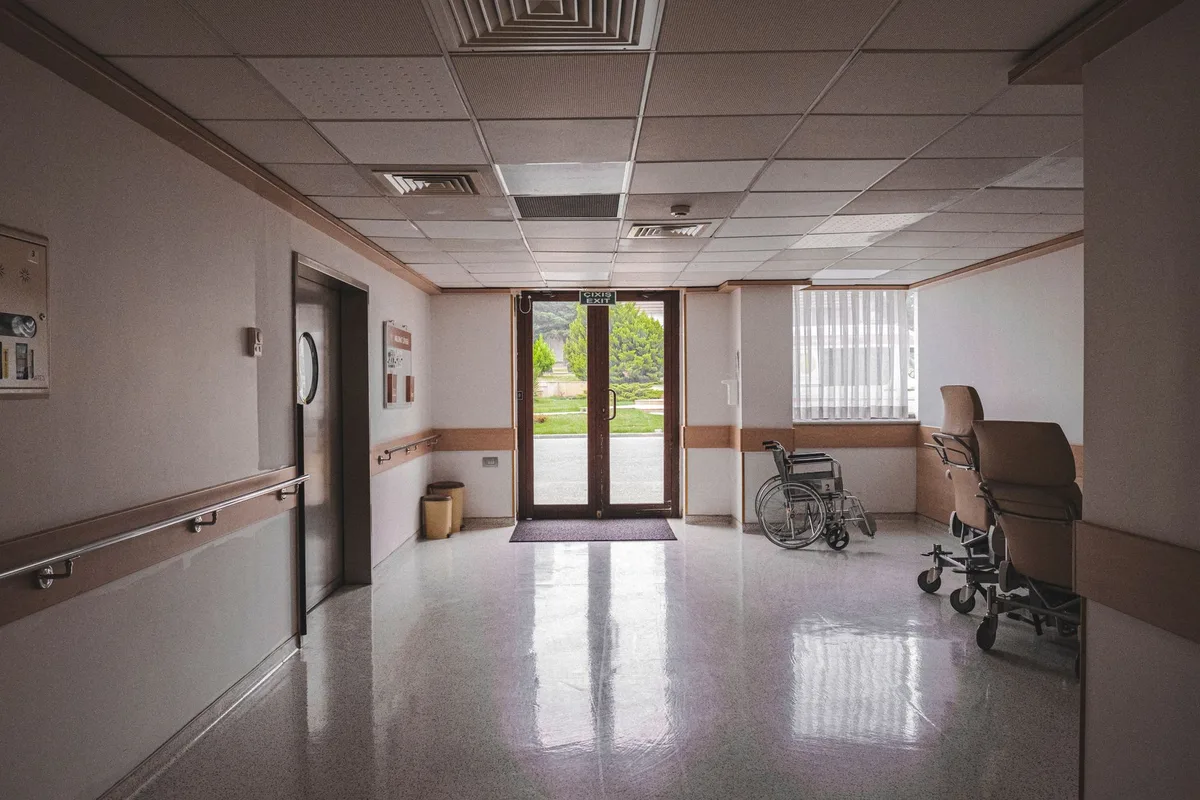 An empty hospital corridor at night in hard monochrome, lit from the far end.