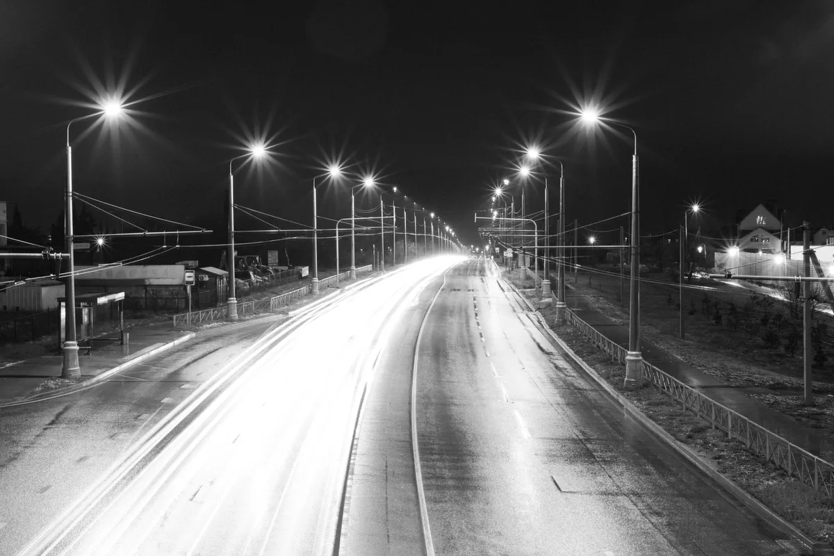 An empty road at night under hard headlights, photographed in high-contrast monochrome.