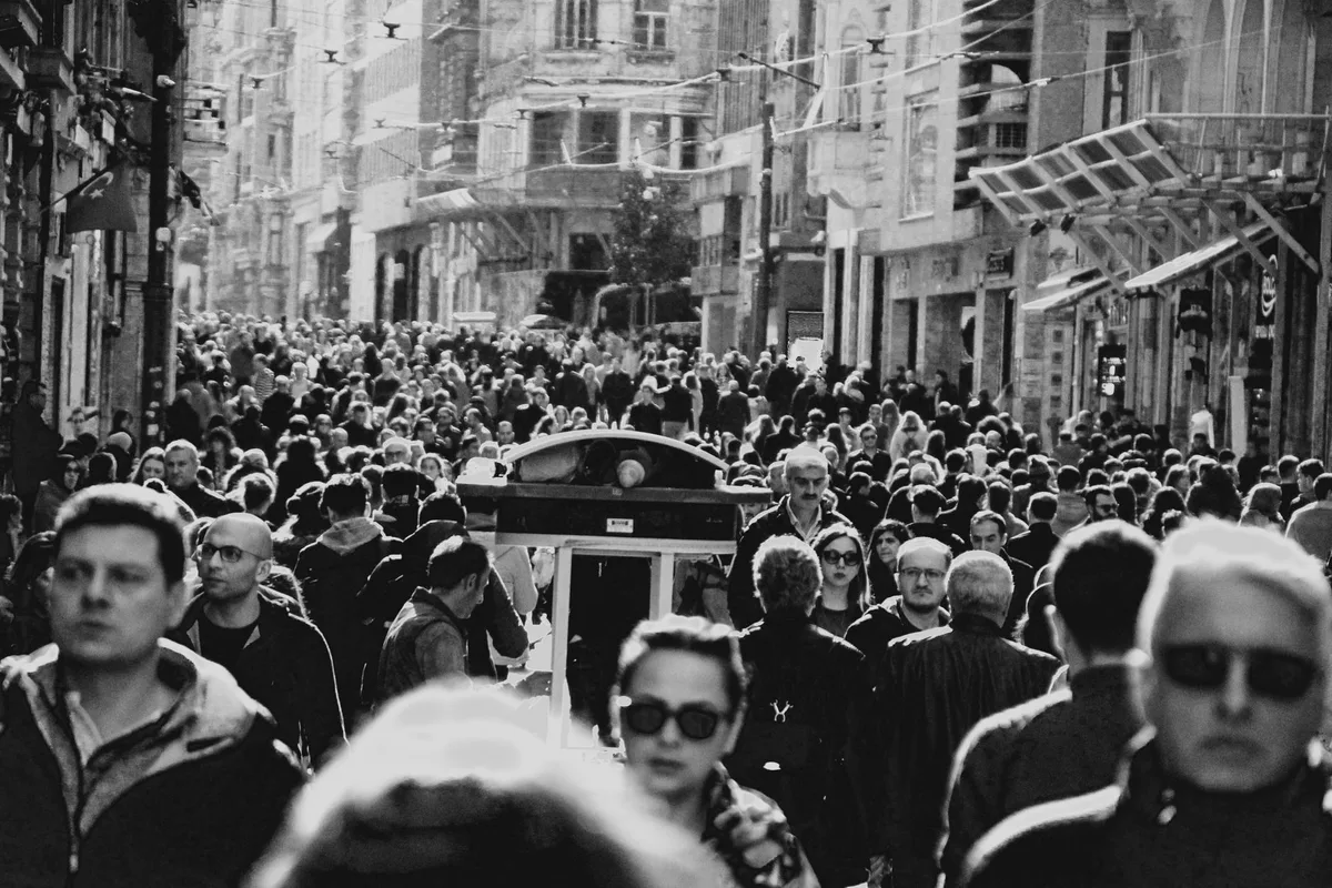 A crowded street photographed in hard black and white, faces indistinct.