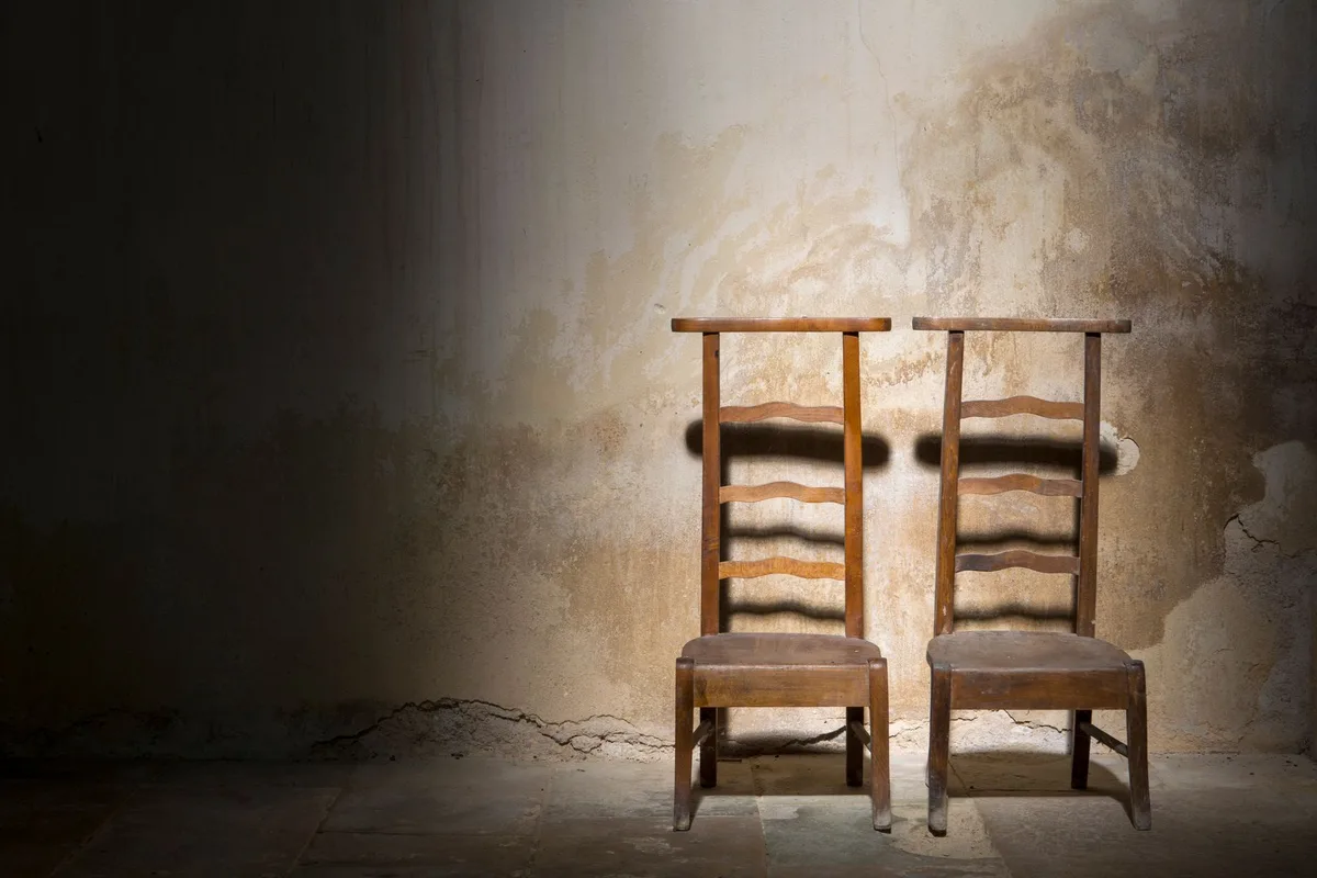 Two empty chairs in a dark room, lit from a single side.